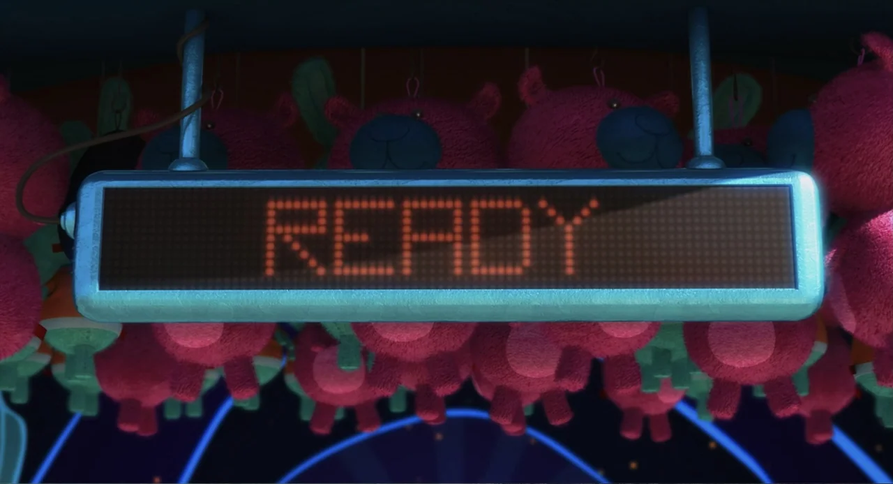 Despicable Me (2010) movie still: closeup — A horizontal metal-framed digital display sign is surrounded by rows of pink plush bears. The screen…