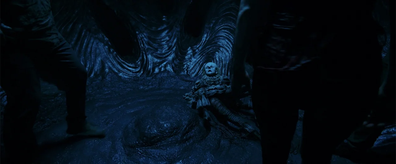 K.G.F: Chapter 2 (2022) movie still: medium — A dark subterranean space features swirling organic wall textures and a central dirt mound. A costumed…