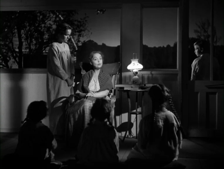 The Night Of The Hunter (1955) movie still: medium — An enclosed porch at night features a group of children gathered around an adult. An elderly…