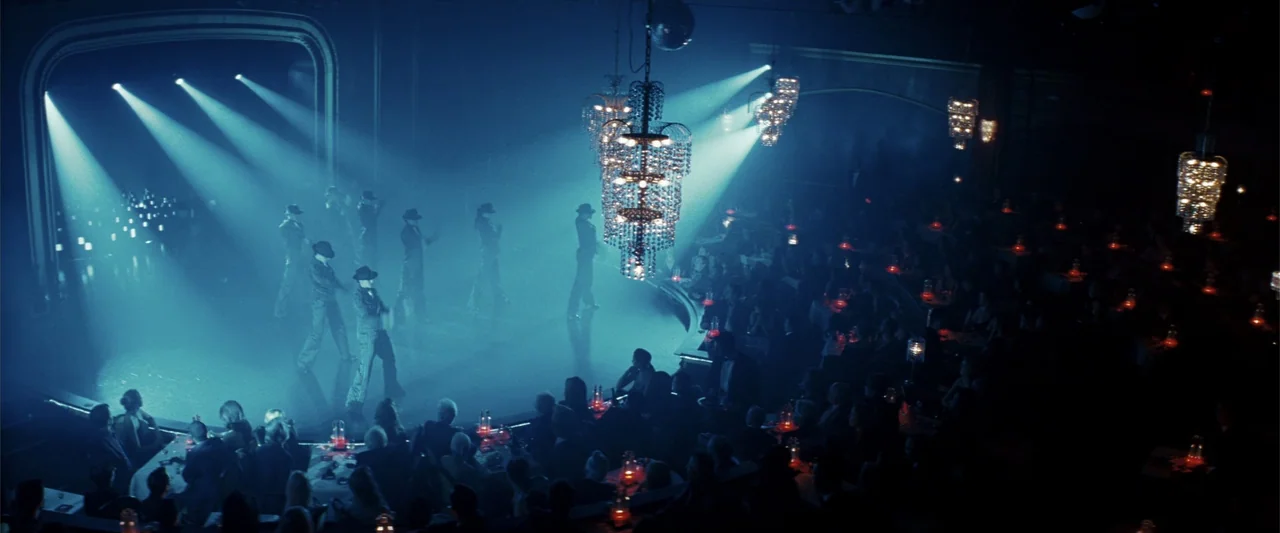 Rush Hour 3 (2007) movie still: wide — A dimly lit nightclub features a central dance stage under cool blue theatrical lighting. Dancers in period…