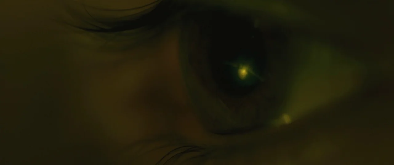 Evolution (2015) movie still: closeup — A dark environment holds a close-up of an eye reflecting a tiny light. The iris contains a small bright…