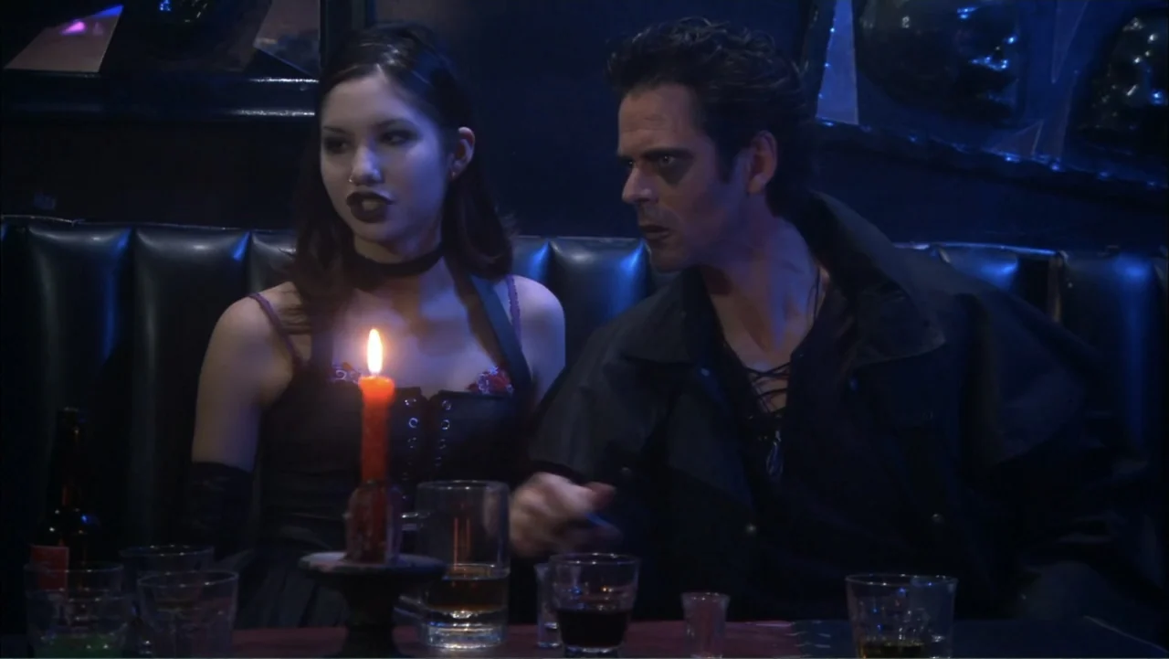 O código oculto (2025) movie still: medium — A dark bar booth features a black leather bench and a wooden table. A man and a woman sit together…