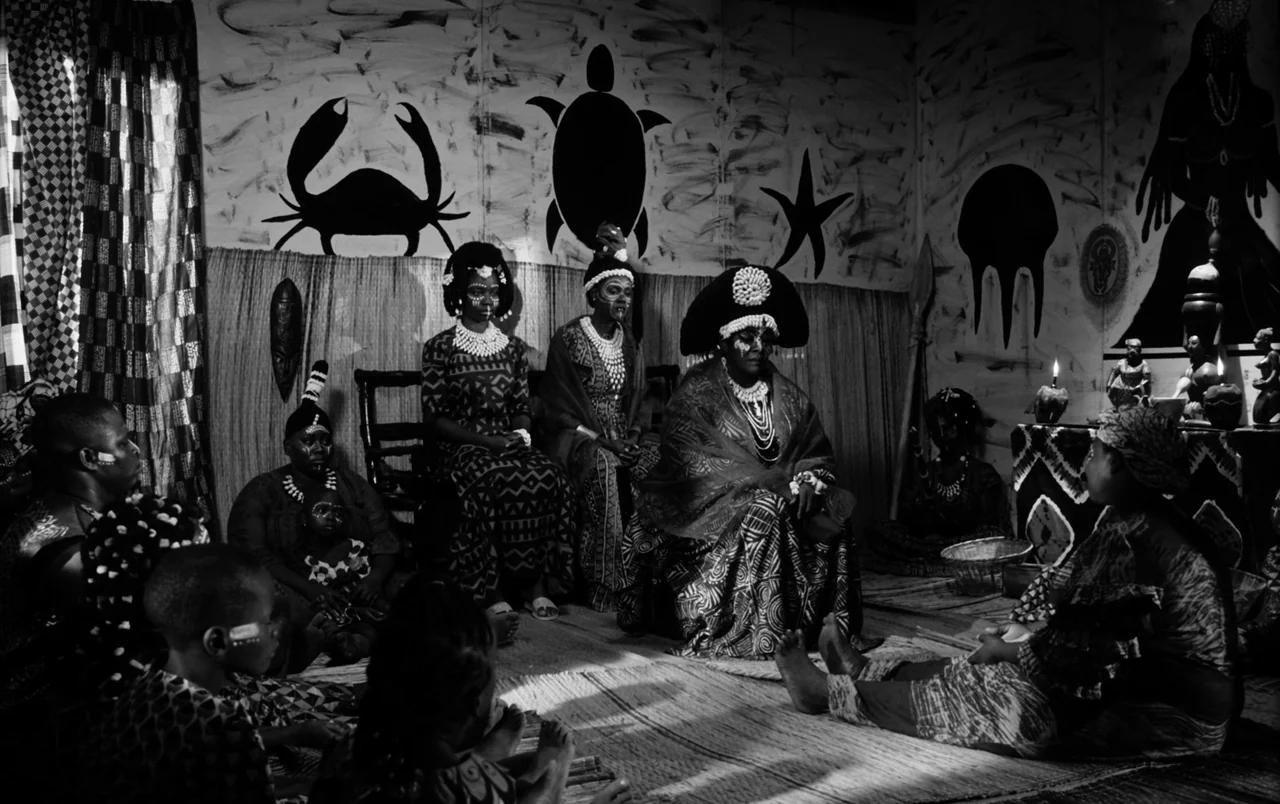 Mami Wata (2023) movie still: fullbody — An interior space features walls painted with silhouettes of a crab, turtle, and starfish. A group of…
