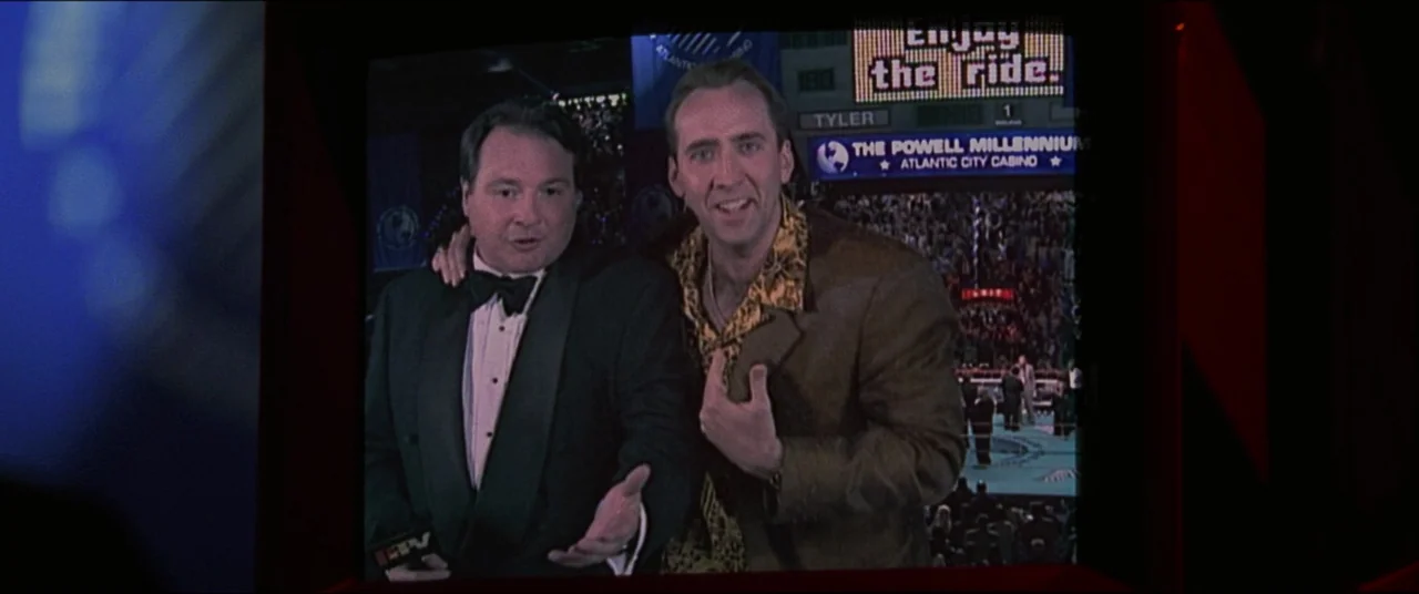 Snake Eyes (1998) movie still: medium — Two men stand in front of a digital screen depicting a crowded boxing arena. The image appears as a…