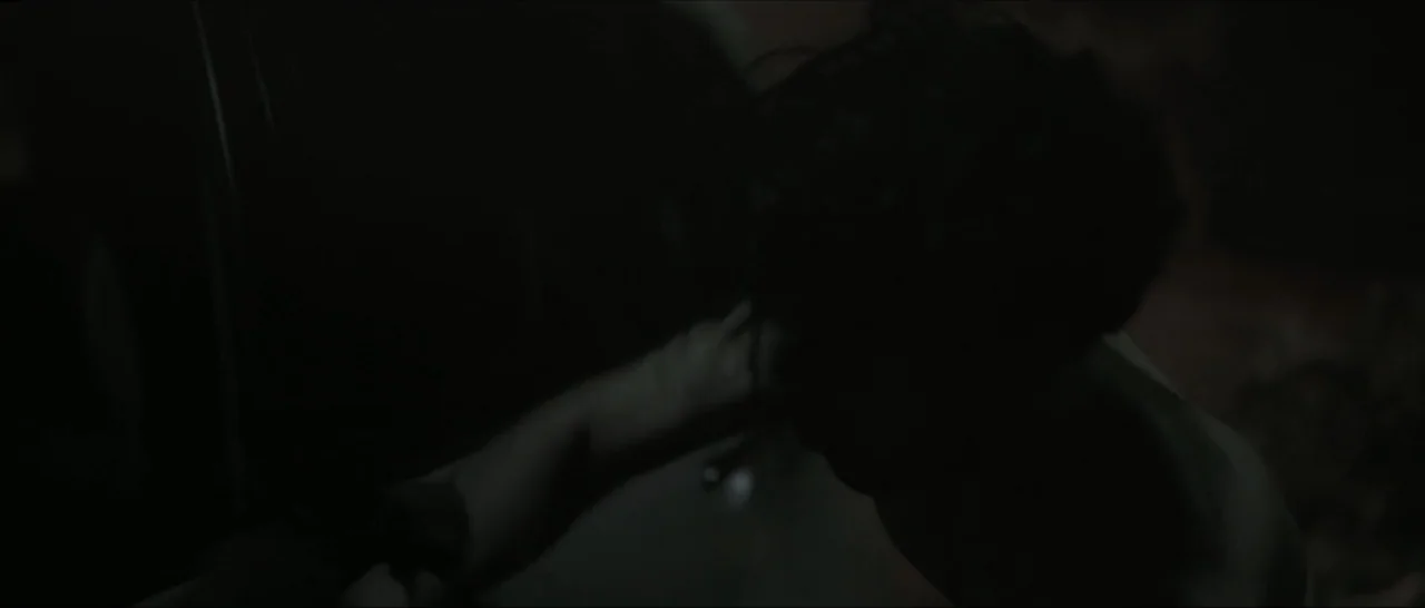 Innocent Vengeance (2023) movie still: medium — A dark, dimly lit interior space with shadows obscuring most architectural details. A person reaches…