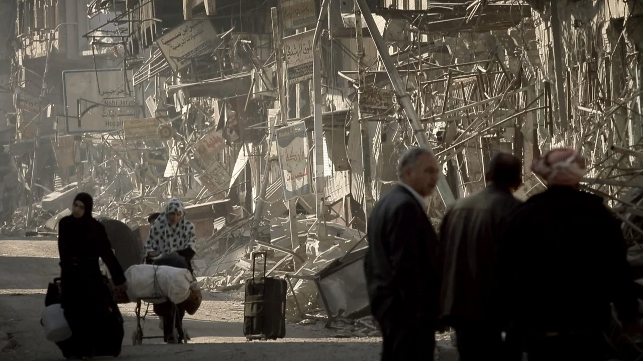 City of Two Springs (2019) movie still: wide — A devastated urban street is filled with structural rubble and hanging metal debris. Several people…