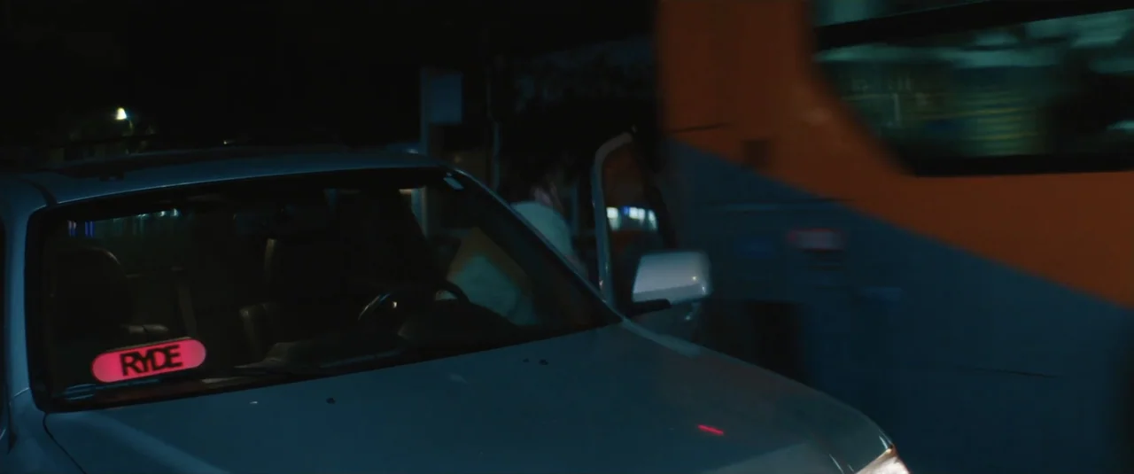 Stalker (2020) movie still: medium — A dark night street setting features a stationary car with a glowing sign inside. A person sits in the driver…