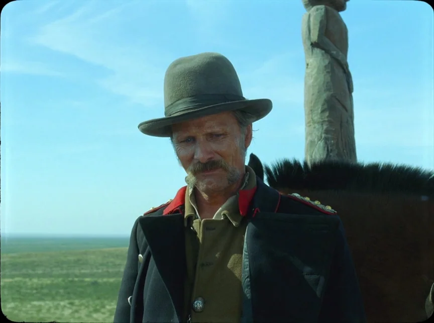 Jauja (2014) movie still: medium — A vast, flat grassy plain stretches toward the horizon under a clear blue sky. A man in a 19th-century military…