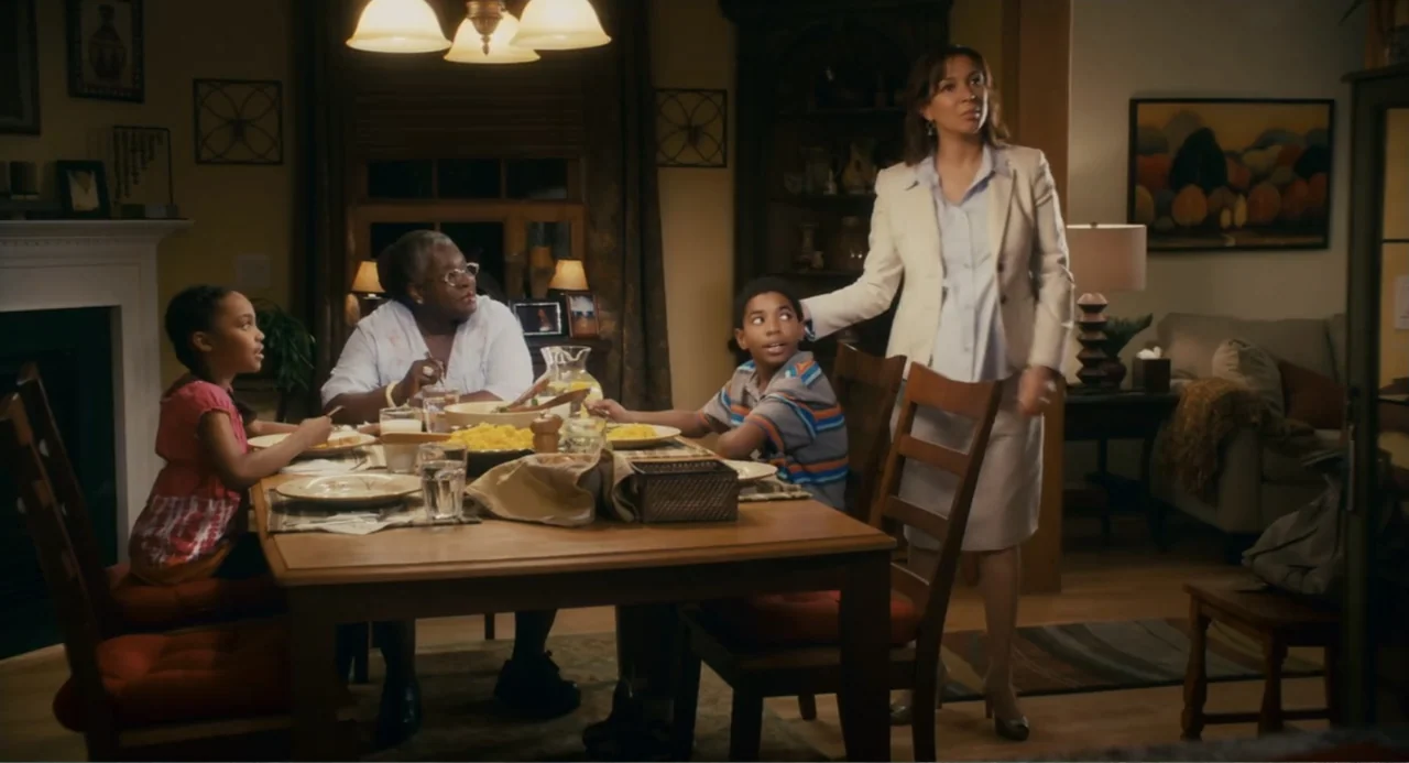Grown Ups (2010) movie still: medium — A well-lit residential room features a wooden table set for an evening meal. Three family members sit around…