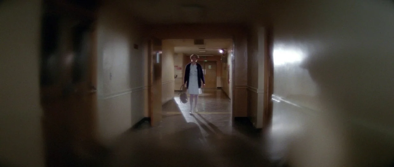 Halloween II (1981) movie still: wide — A long, dimly lit hospital corridor with cream-colored walls and polished linoleum floors. A woman in a…
