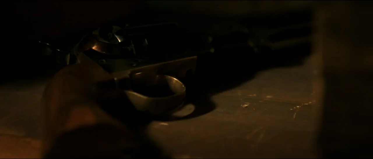 Dead for a Dollar (2022) movie still: closeup — A dark wooden surface holds a vintage metal revolver in low light. The weapon rests silently on the…