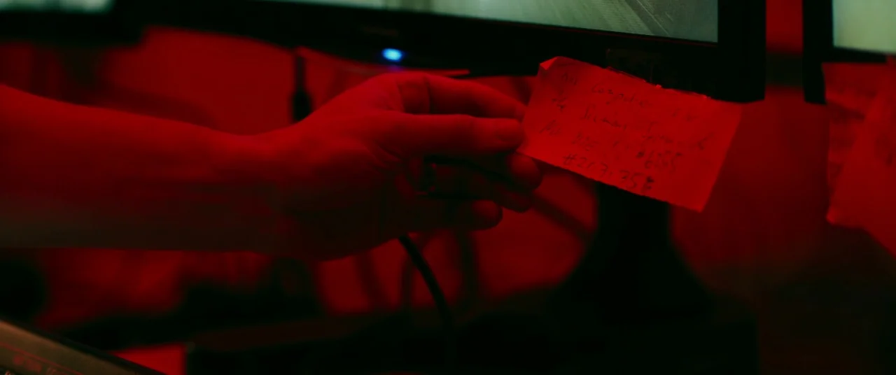 Ready or Not (2019) movie still: closeup — A dark space features computer monitors emitting a strong red light in the darkness. A hand is visible…