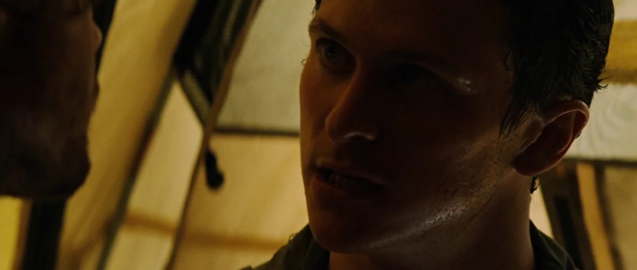 The Ruins (2008) movie still: closeup — An interior of a canvas tent illuminated by dim, warm ambient light. A man with a strained expression gazes…