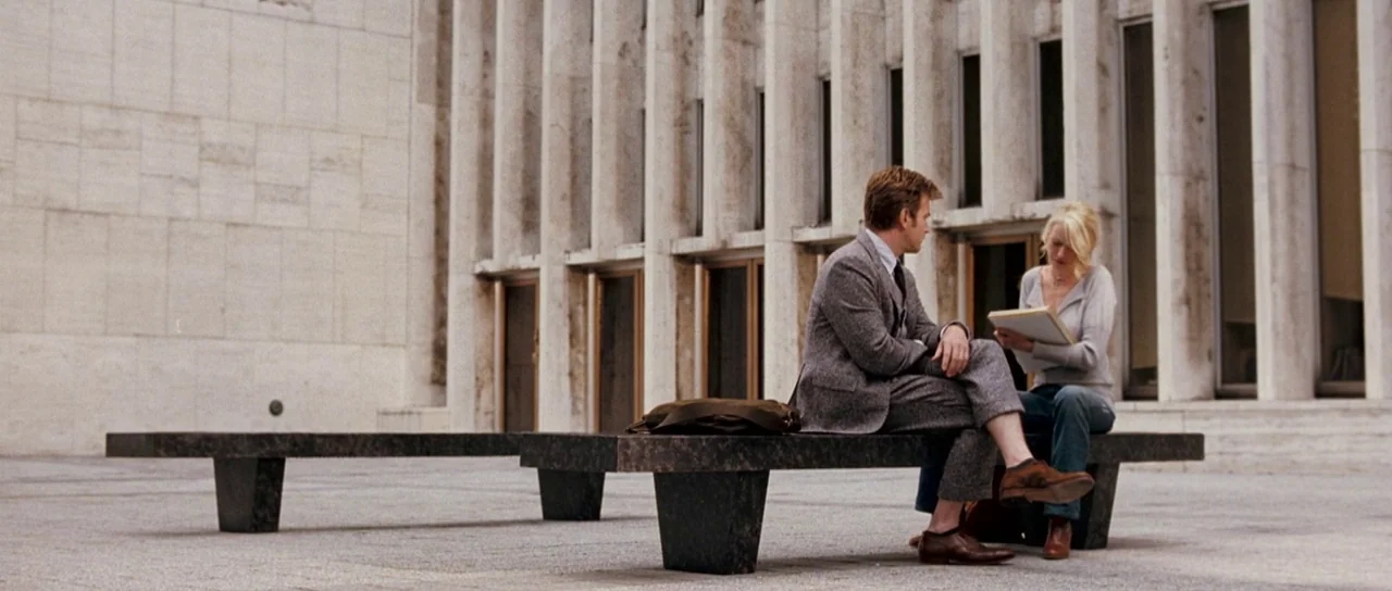 Stay (2005) movie still: wide — A modern plaza with large marble-like vertical columns and smooth stone paving. A man and a woman sit on a long dark…