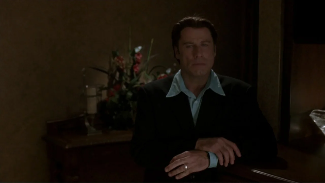 The Punisher (2004) movie still: medium — A dimly lit interior room features a floral arrangement on a wooden console table. A man in a dark suit…
