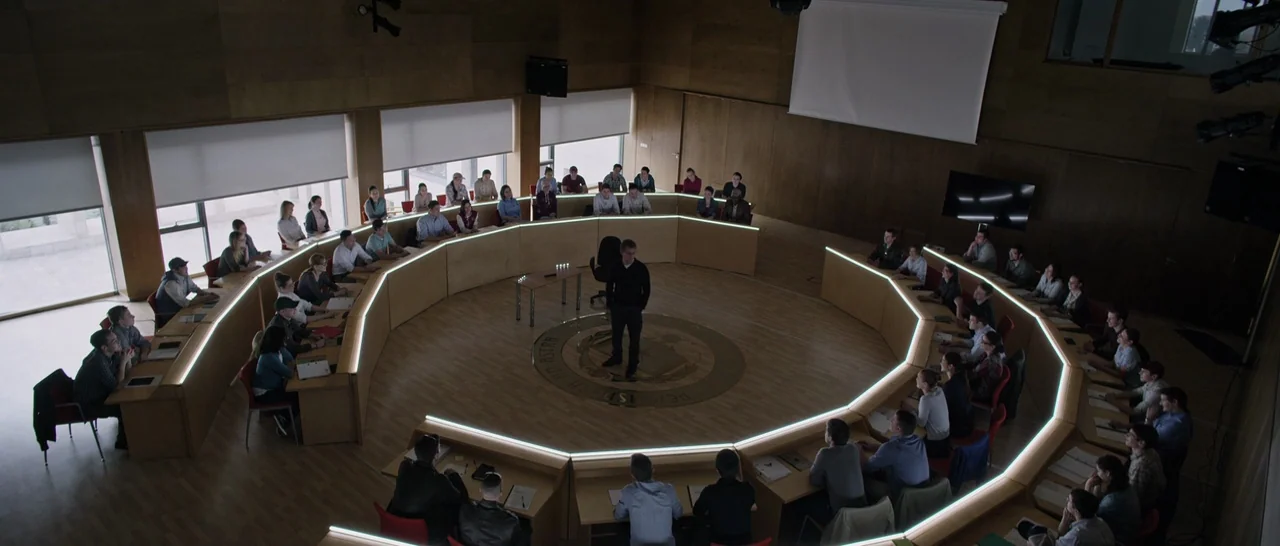 The Martian (2015) movie still: wide — A circular wooden lecture hall features tiered seating arranged around a central floor area. A lone man…