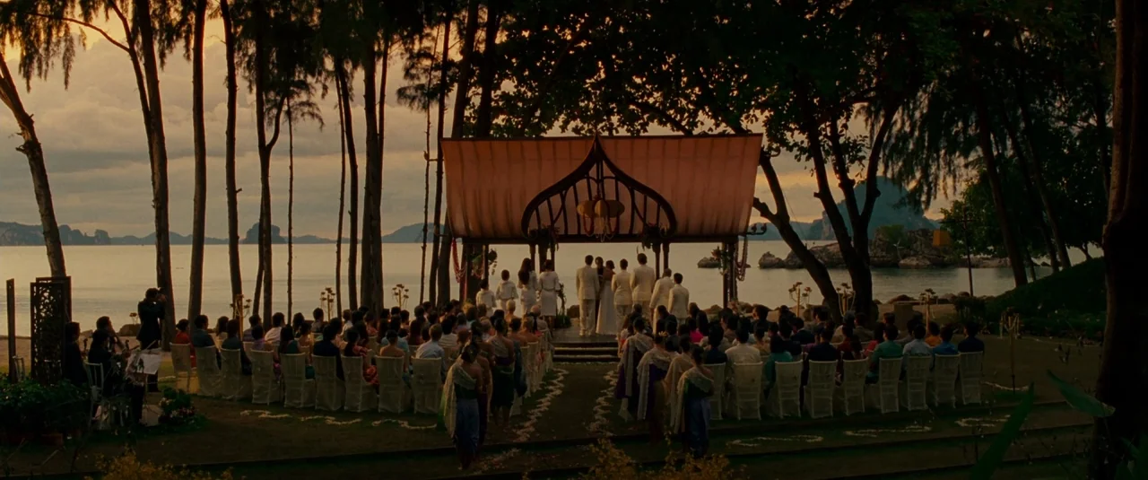 The Hangover Part II (2011) movie still: wide — A beachside wedding ceremony takes place under a wooden pavilion at golden hour. Guests sit on rows…