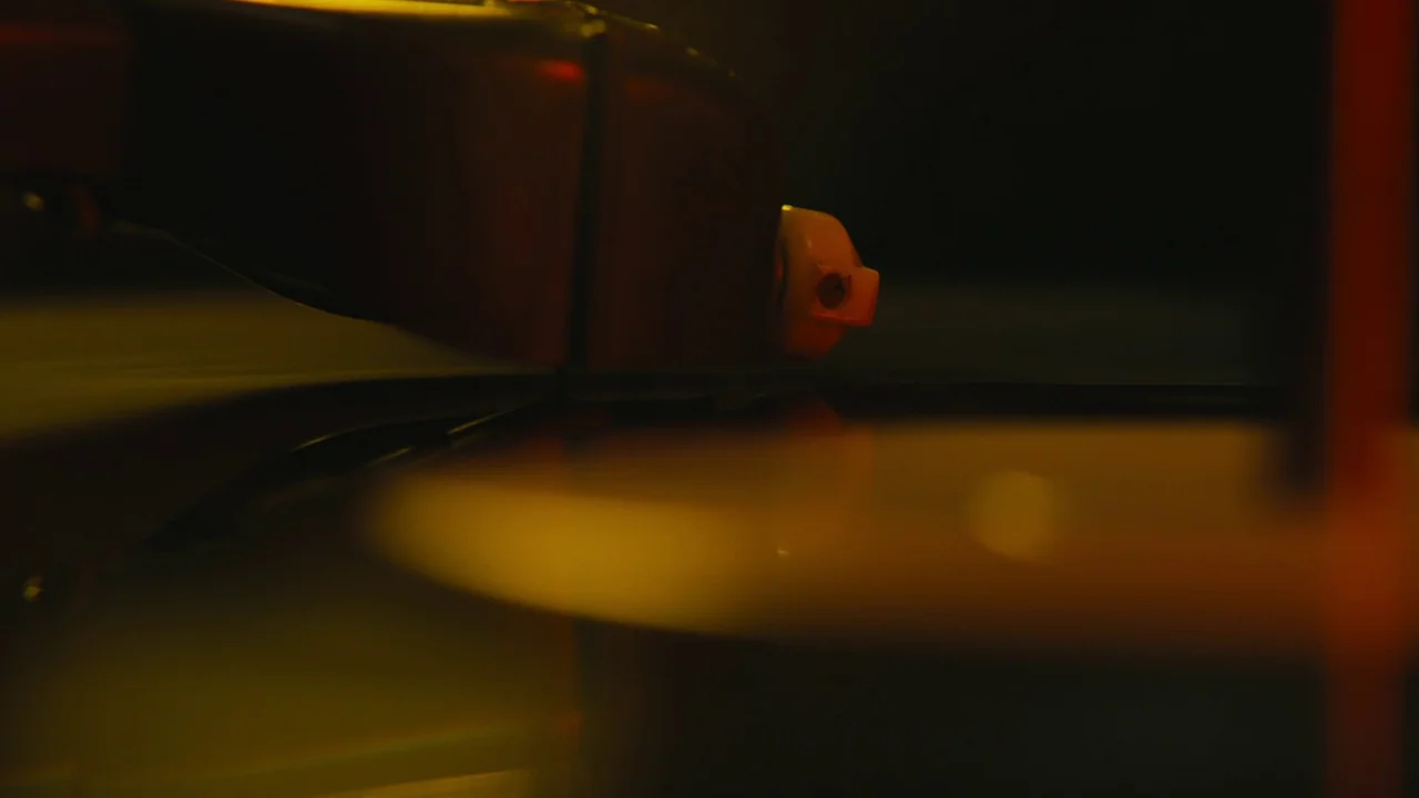 Lover’s Rock (2020) movie still: closeup — A close-up view shows the tone arm and stylus resting on a vinyl record. The equipment is illuminated by…