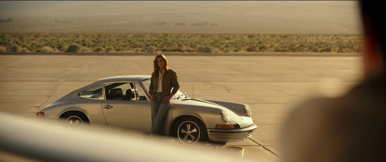 Top Gun: Maverick (2022) movie still: wide — A vast, empty desert tarmac stretches toward a distant, low-lying horizon line. A woman leans against…