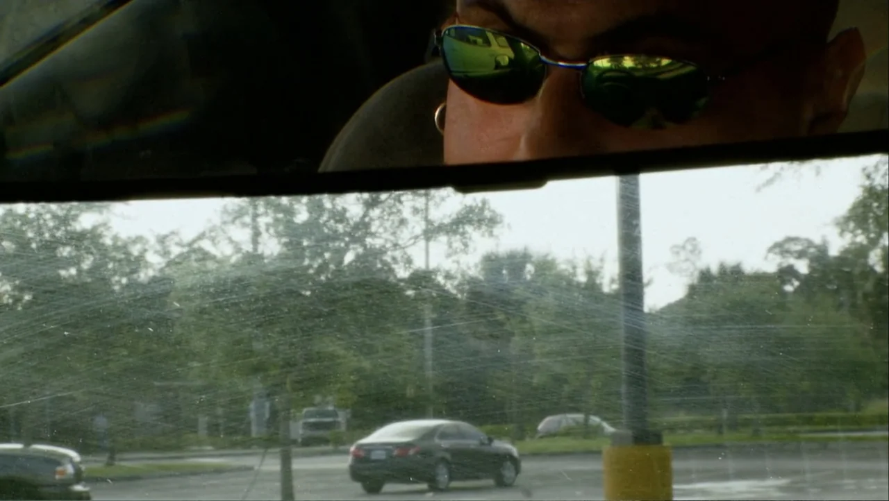 12th & Delaware (2010) movie still: closeup — A view through a streaked car windshield shows a parking lot with trees. The reflection in the…