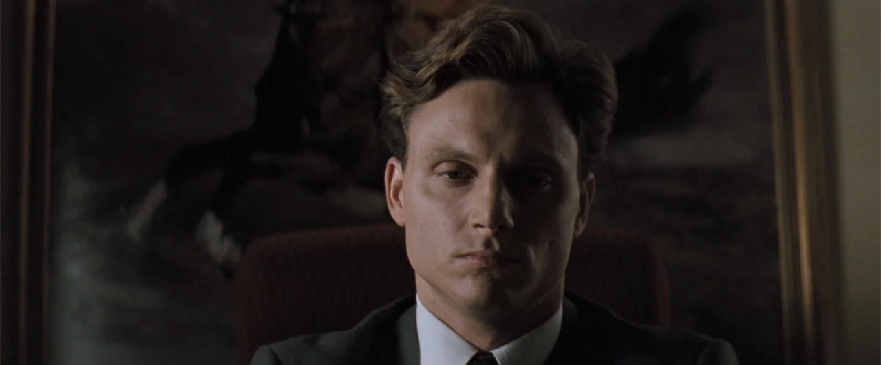 The Pelican Brief (1993) movie still: closeup — An interior office space features a dark chair and a framed painting behind him. A man in a suit…