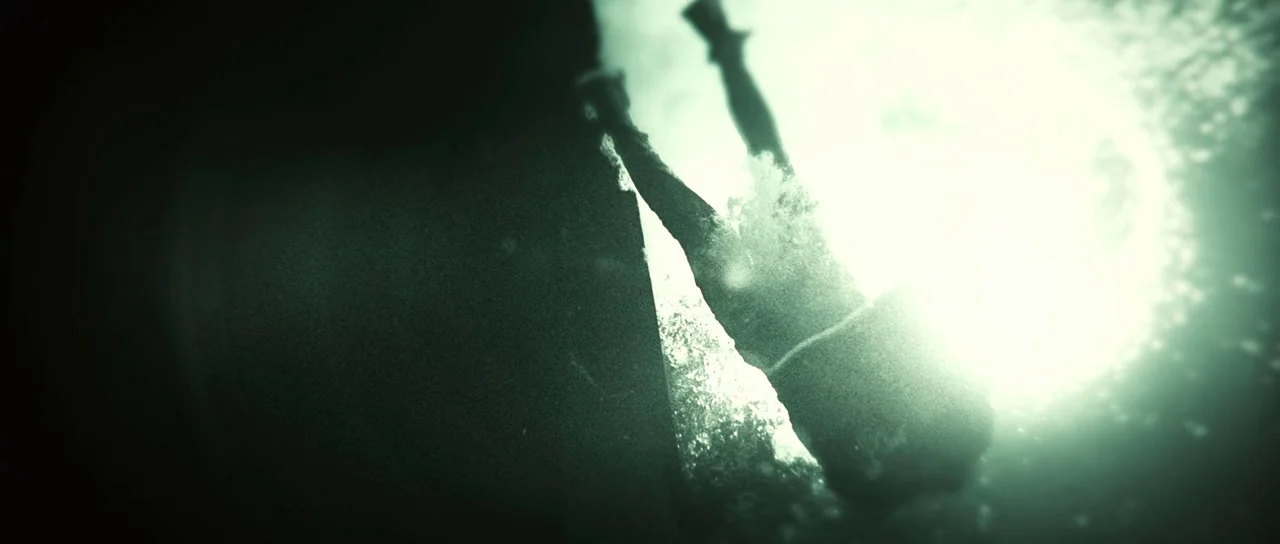 Daybreakers (2009) movie still: wide — A person is captured from below while swimming through deep, clear turquoise-tinted water. Bright sunlight…