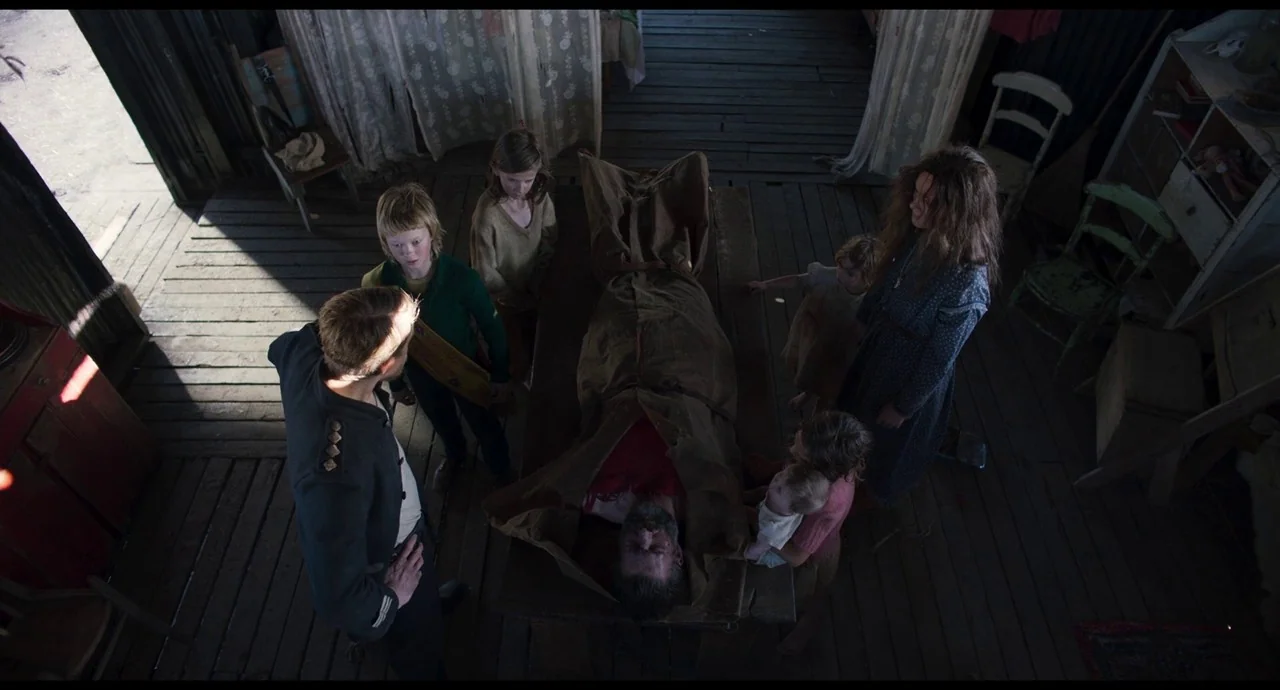 True History of the Kelly Gang (2019) movie still: wide — A rustic wooden shack with weathered floorboards serves as the setting for the family. A…