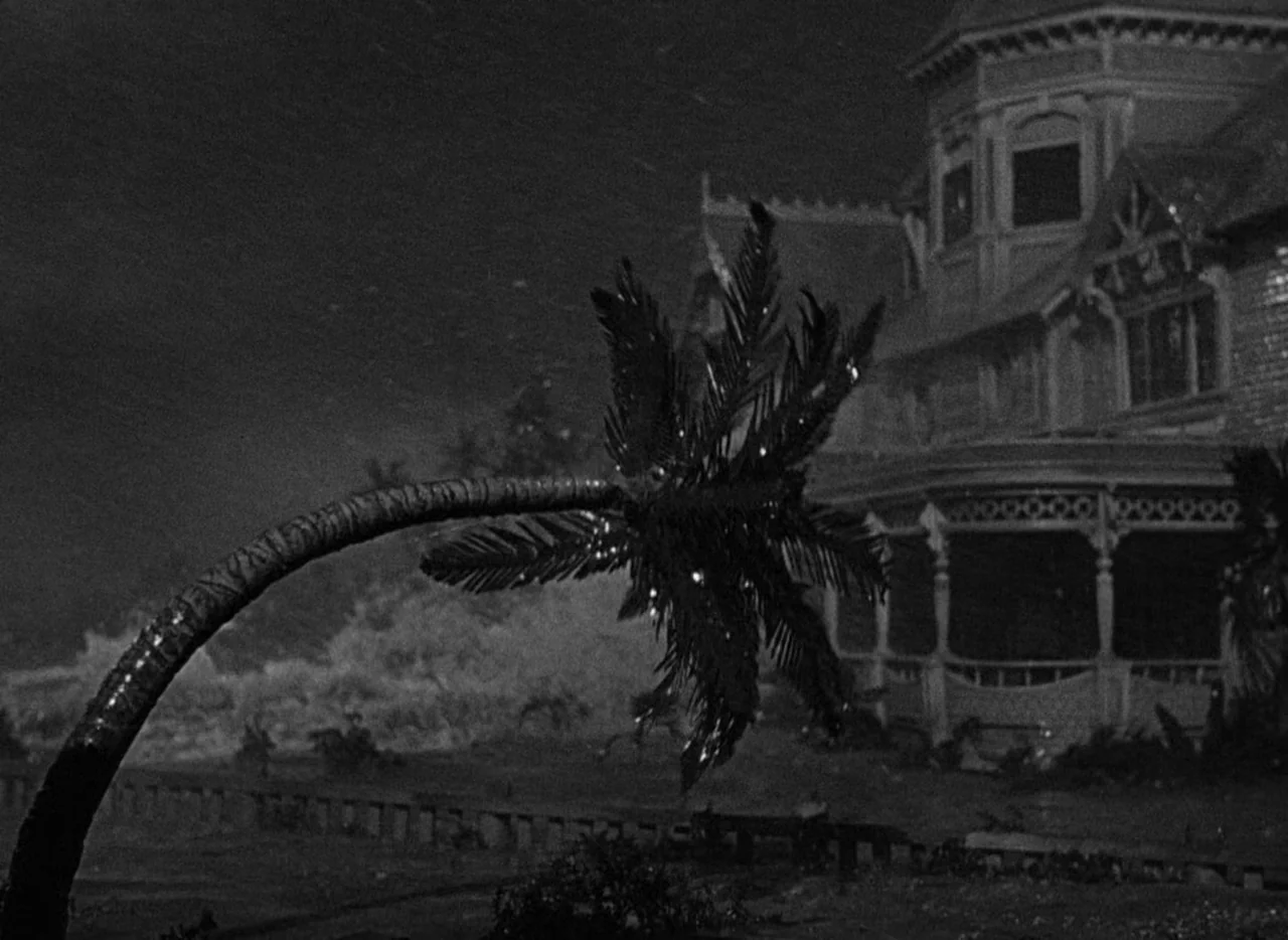 Key Largo (1948) movie still: establishing — A dark, storm-swept coastal property features a grand Victorian house behind a bending palm tree. Wind…
