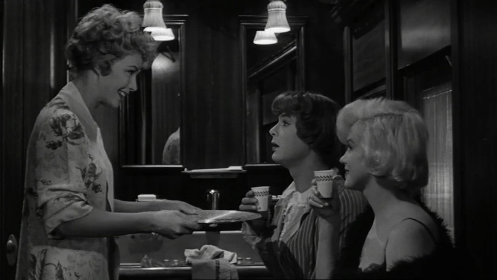 Some Like It Hot (1959) movie still: medium — A cramped wood-paneled train washroom features a central mirror and mounted light fixtures. Three…