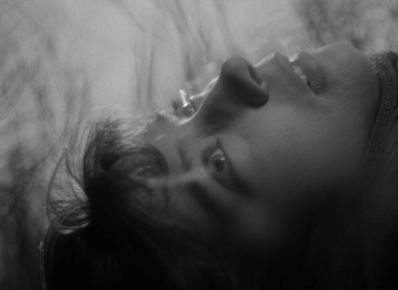 Letter Never Sent (1960) movie still: closeup — A person lies on their back in an outdoor field. Dark grass or foliage blurs across the foreground…