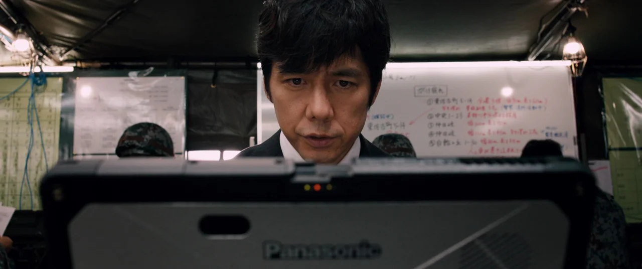 Shin Ultraman (2022) movie still: closeup — A dark command center features a large white magnetic board covered in handwritten notes. A man leans…