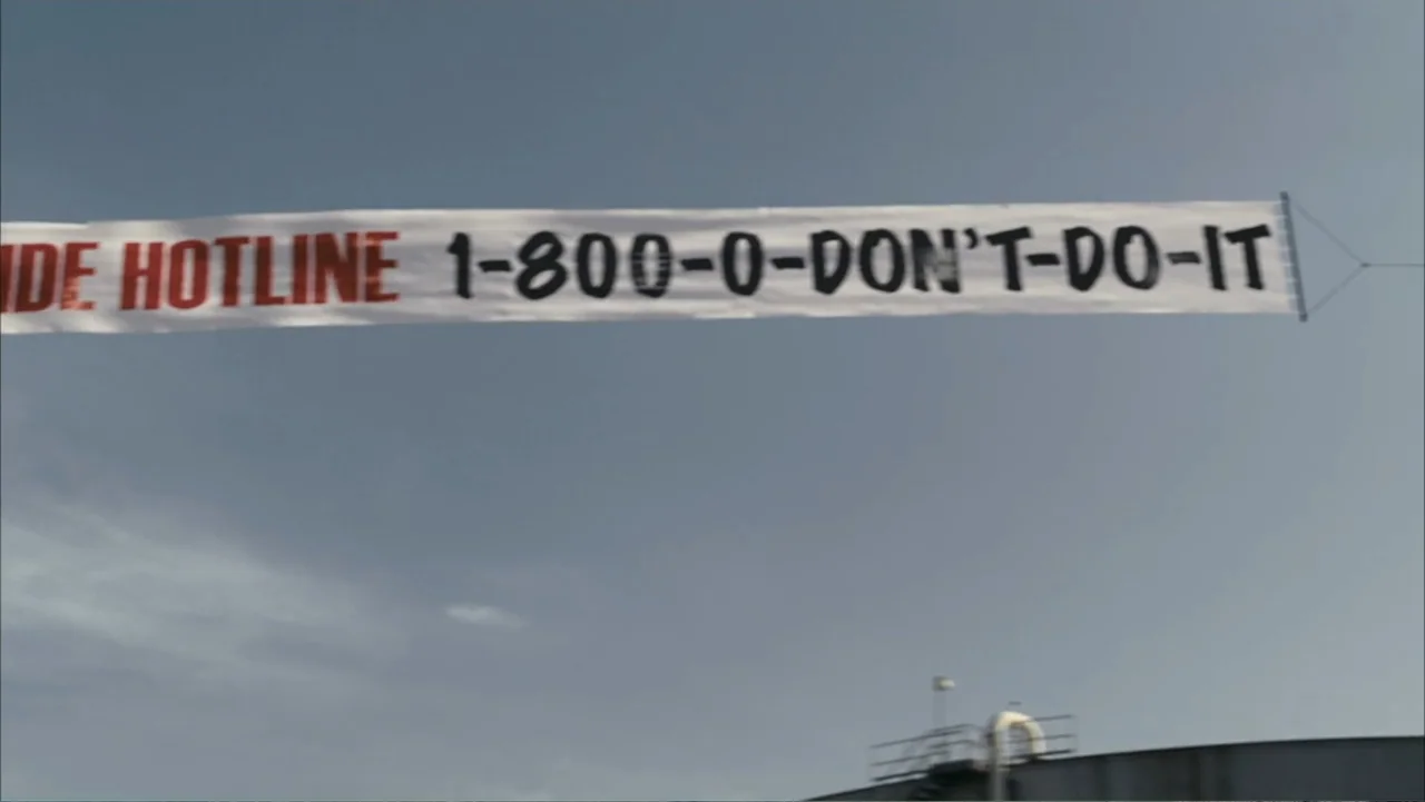 Get Smart (2008) movie still: wide — A long white banner with black and red text hangs against a clear sky. A concrete rooftop structure is visible…