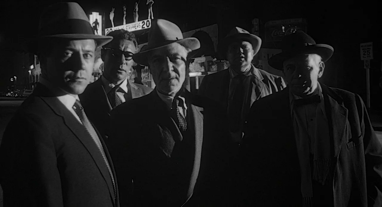 Touch of Evil (1958) movie still: medium — Five men in hats and suits stand closely together on a dark city street at night. The group stares toward…