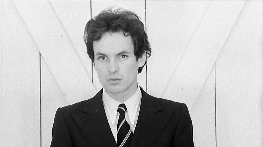 Love Is Colder Than Death (1969) movie still: medium — A man stands before a white paneled door with diagonal structural supports. He is positioned…