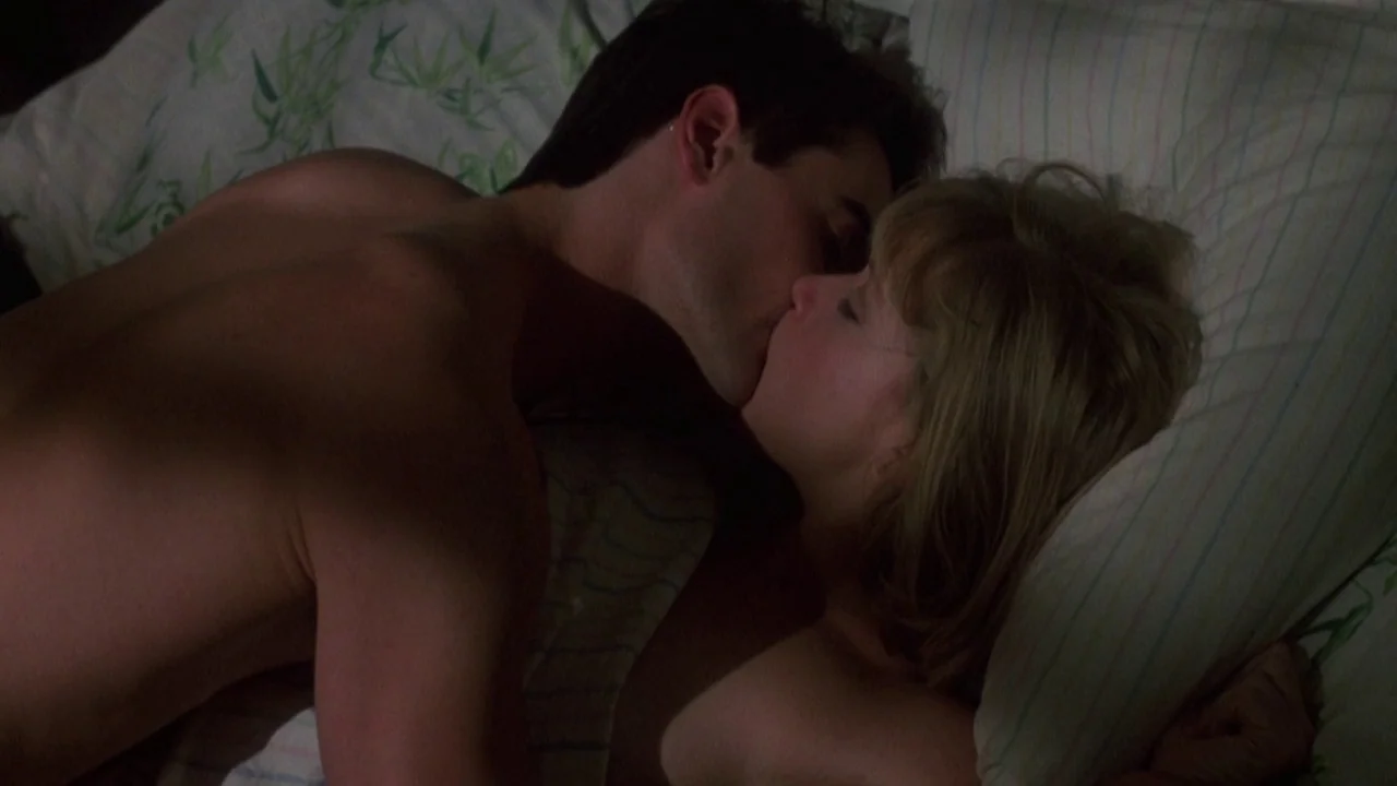 Re-Animator (1985) movie still: closeup — A dark bedroom setting where two people are lying close together on a pillow. A shirtless man leans over a…