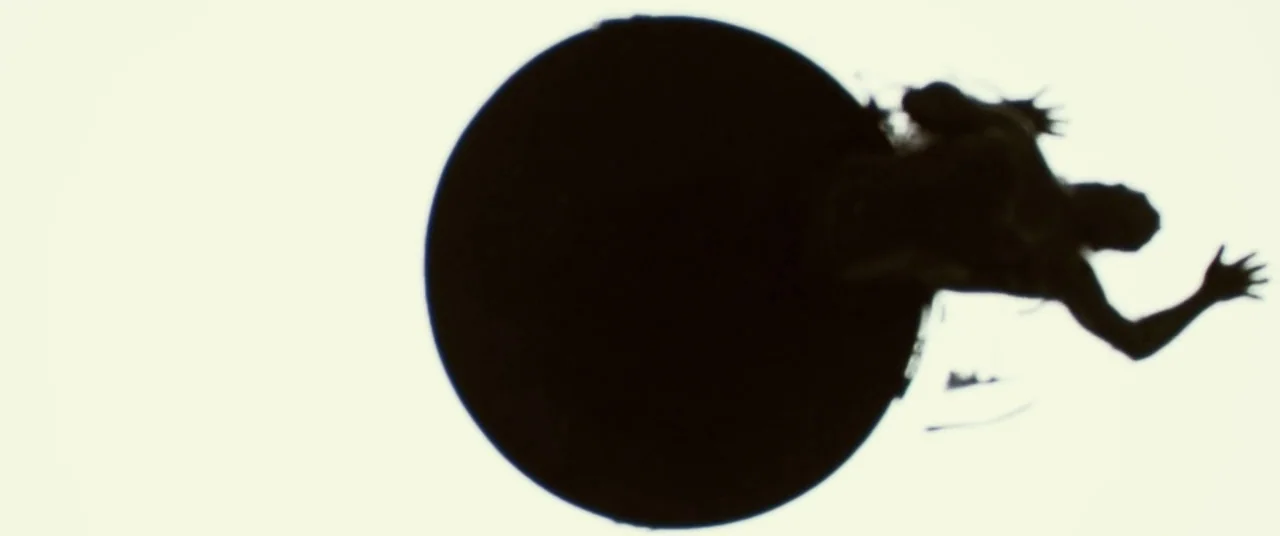 Beyond The Black Rainbow (2010) movie still: wide — A dark circular shape dominates the frame against a featureless bright white background. A human…