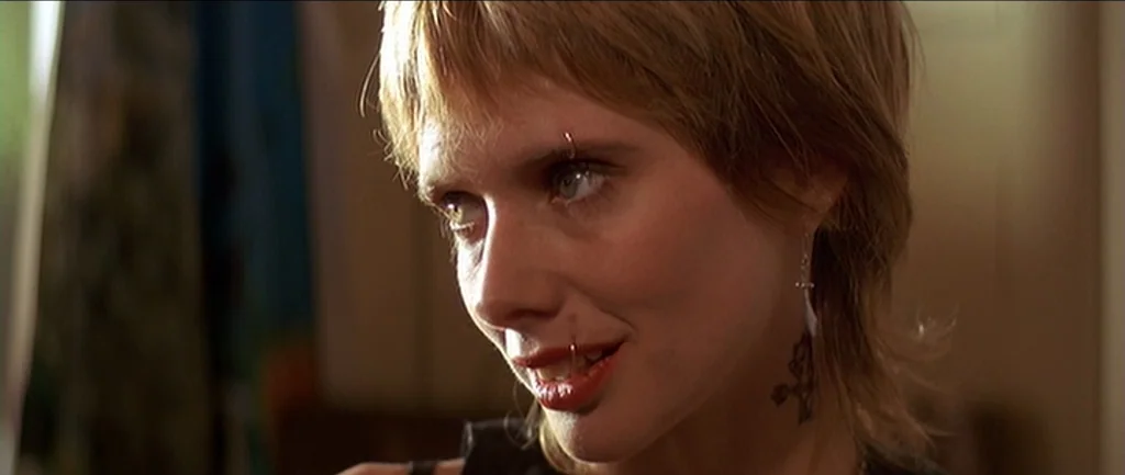 Pulp Fiction (1994) movie still: closeup — The frame shows a close-up portrait of a young woman inside an indoor space. She has short hair and…