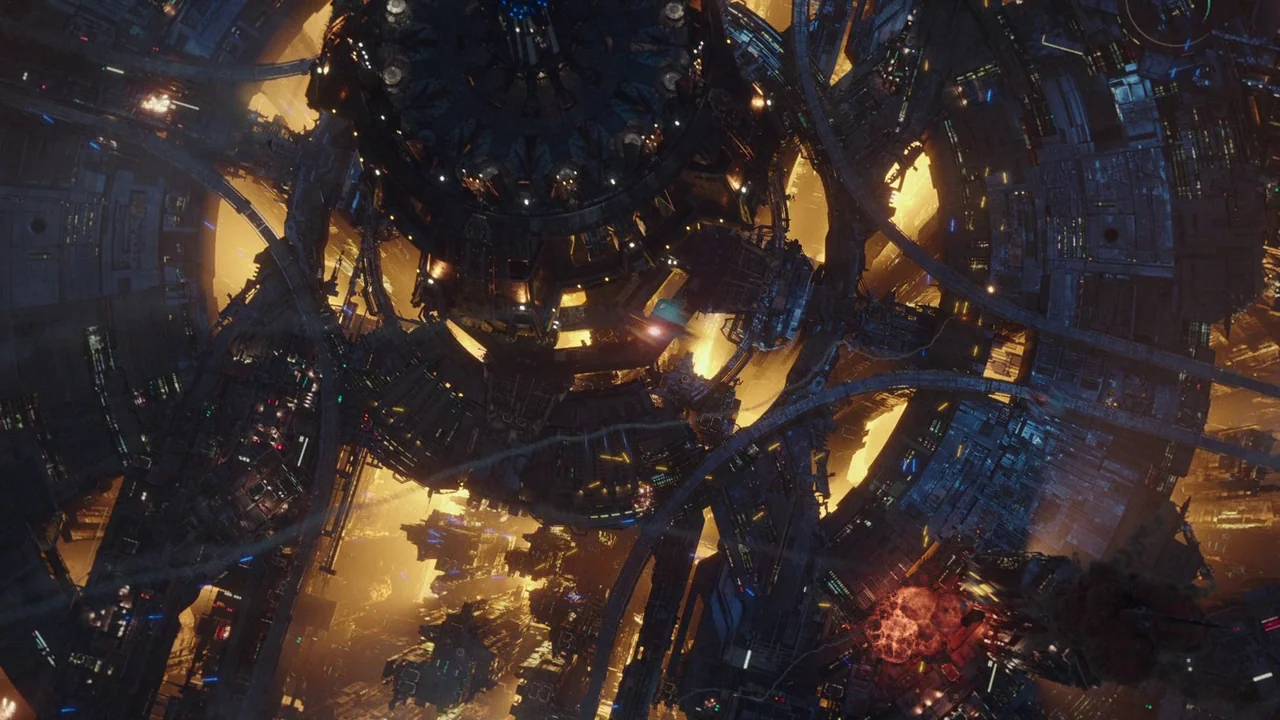 Bumblebee (2018) movie still: establishing — A massive, complex orbital space station is surrounded by smaller ships and fiery explosions. The dark,…