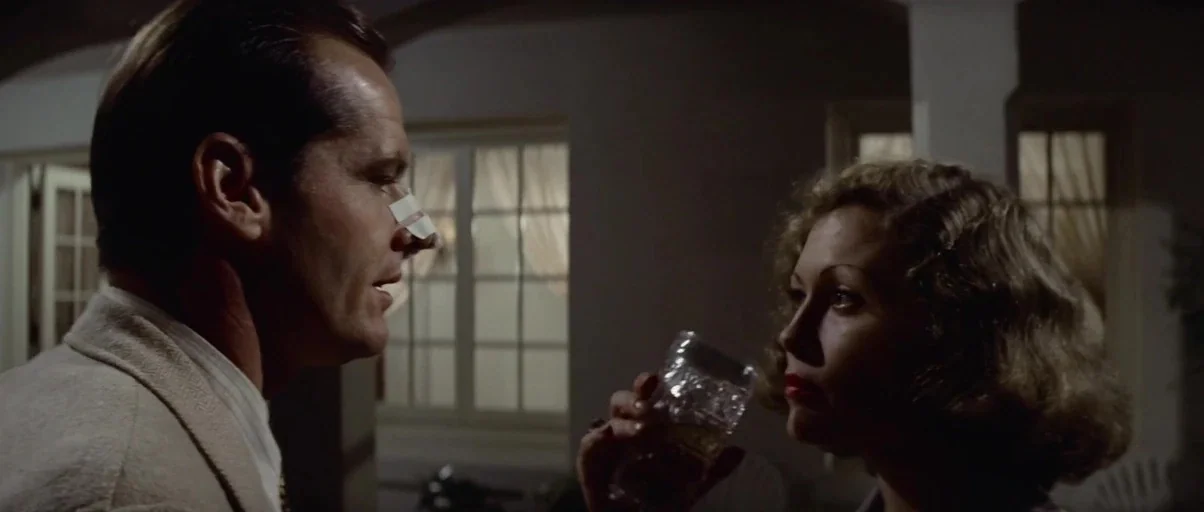 Chinatown (1974) movie still: medium — A dimly lit covered outdoor area features white structural columns and large window panes. A man with a…