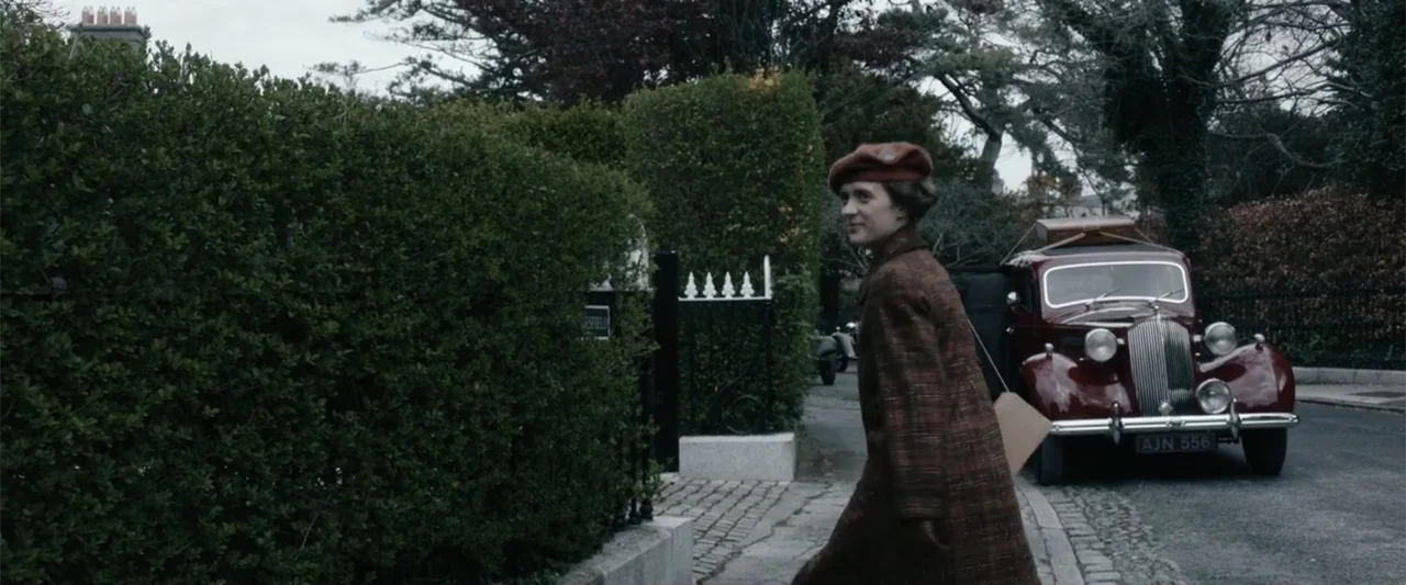 Freud's Last Session (2023) movie still: fullbody — A quiet residential street in the 1930s lined with tall hedges and cobblestone pavement. A woman…