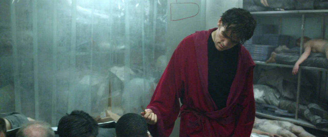 The House That Jack Built (2018) movie still: medium — A sterile morgue features metal shelves holding bodies under thin plastic curtains. A man in…