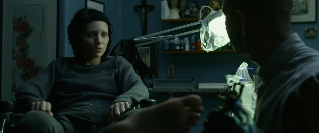 The Girl With The Dragon Tattoo (2011) movie still: medium — A dim room filled with cluttered shelves, a wall crucifix, and framed artwork. A woman…