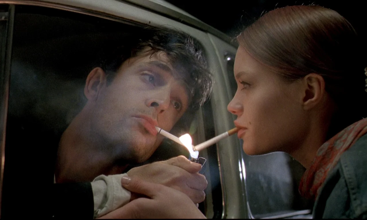 Dellamorte Dellamore (1994) movie still: medium — A dark night setting features two people sharing a light inside a vehicle. The man leans from the…