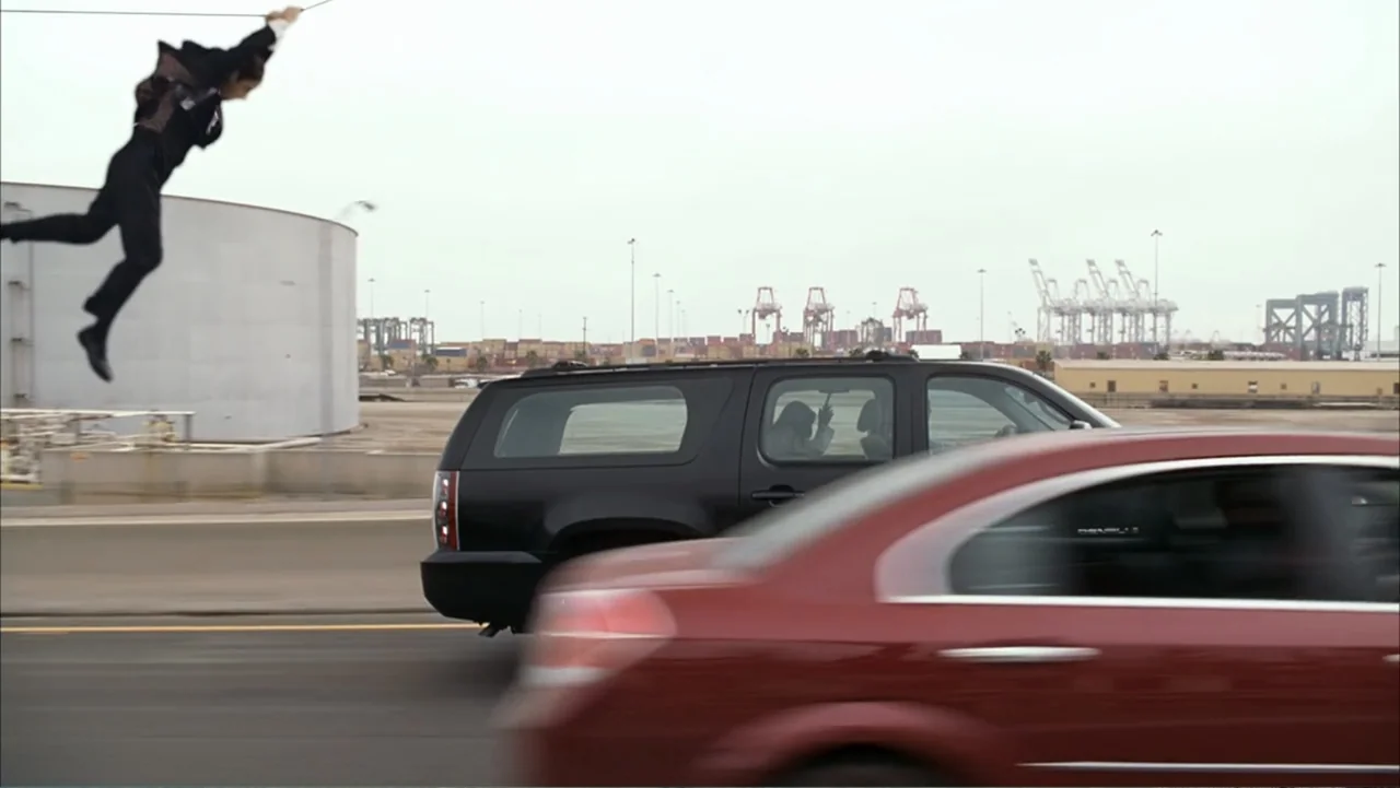 Get Smart (2008) movie still: wide — An industrial shipping yard features cargo cranes, large tanks, and paved asphalt roads. A man in a suit floats…