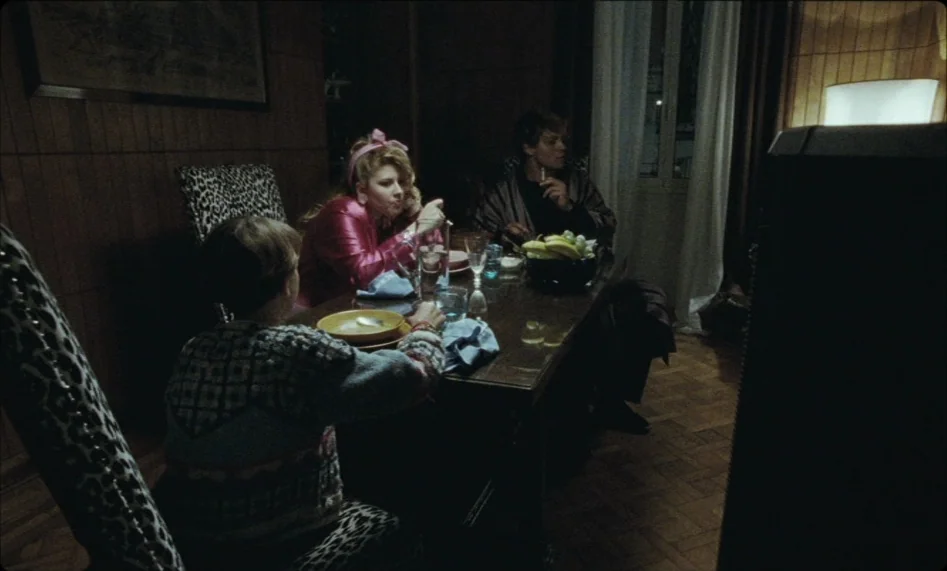Misunderstood (2014) movie still: medium — A dimly lit room features wood-paneled walls and leopard print upholstery on chairs. Three people gather…