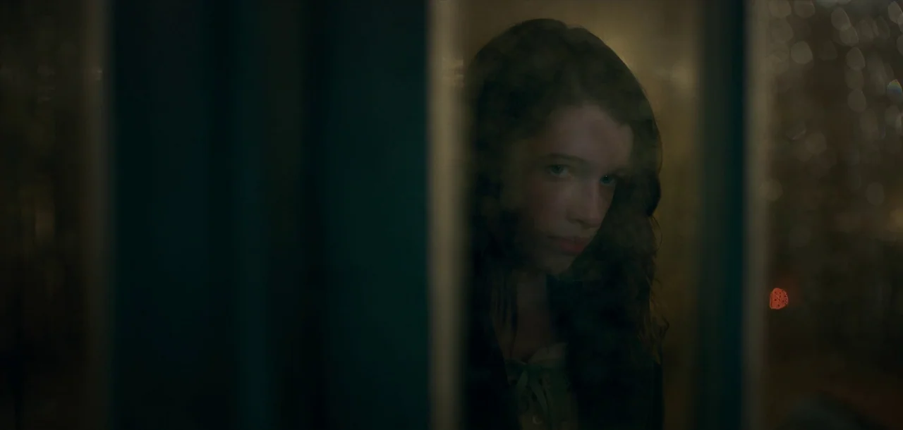 Peter Pan & Wendy (2023) movie still: closeup — A dark, blurred glass surface partially obscures a person looking from the other side. The woman…