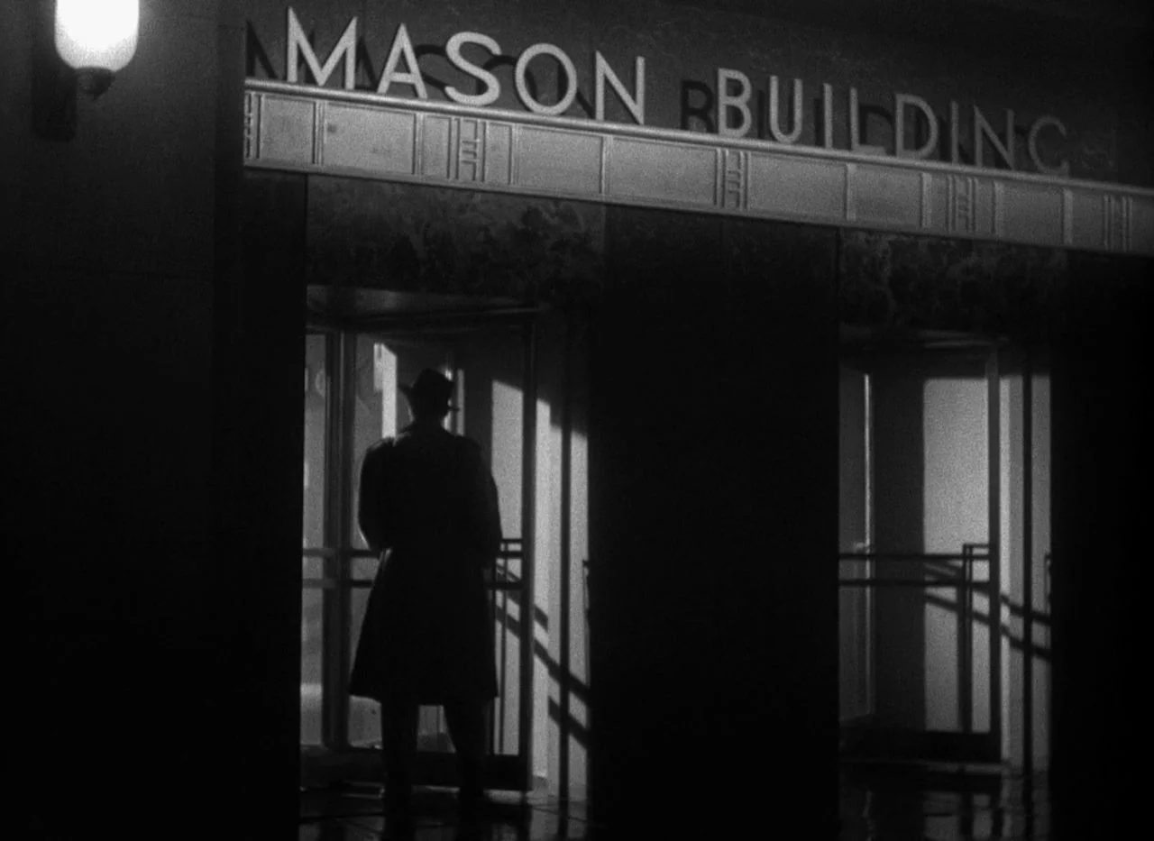Out of the Past (1947) movie still: medium — A stone facade features the text MASON BUILDING above a glass door entrance at night. A silhouette of a…