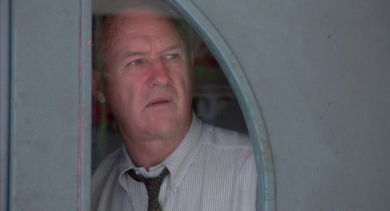Mississippi Burning (1988) movie still: closeup — A man peers through the rounded cutout of a gray painted door frame. He looks slightly away from…