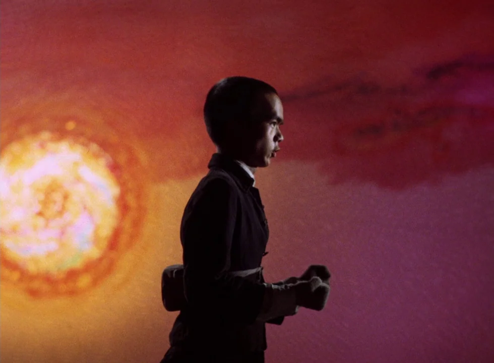 Dodes’ka-den (1970) movie still: medium — A dark figure moves against a wall illuminated by a large, circular projection. The projection features…