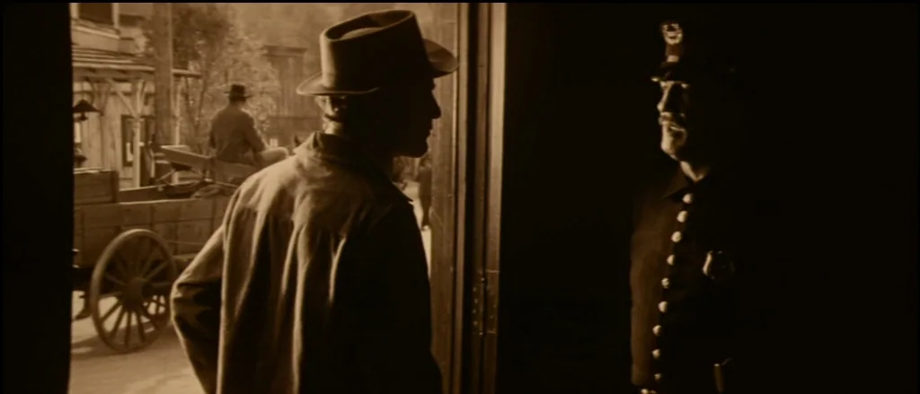 Butch Cassidy and the Sundance Kid (1969) movie still: medium — Two men converse at the threshold of a dark room leading to a street. A horse-drawn…